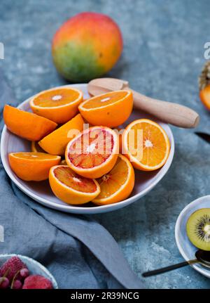 Halved bloody oranges with a wooden juicer on a ceramic plate Stock Photo