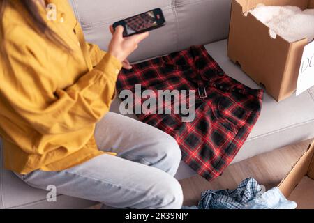 Woman taking photo of skirt at home on smartphone camera for post to sell online on internet market website, selling online ecommerce Stock Photo