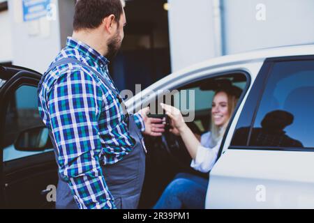 Car service worker taking car keys of woman for providing technical assistance of car Stock Photo