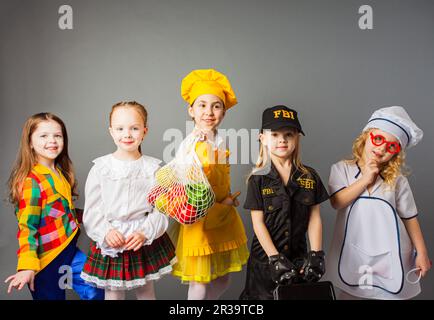 Happy schoolgirls in costumes of different professions isolated on grey background. Stock Photo