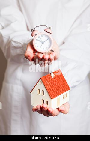 Silhouette of woman holding alarm clock and mockup house Stock Photo