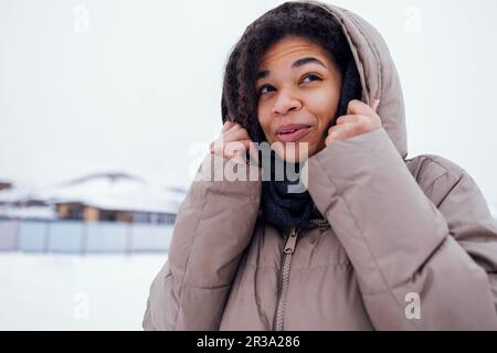 Close up of beautiful mixed race girl feels cold and wraps herself up in knitted woolen scarf. Frozen cute darkskinned young woman in warm casual jack Stock Photo