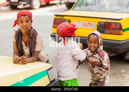 Three small orphan street kids playing and laughing on a quite city road between taxis Stock Photo