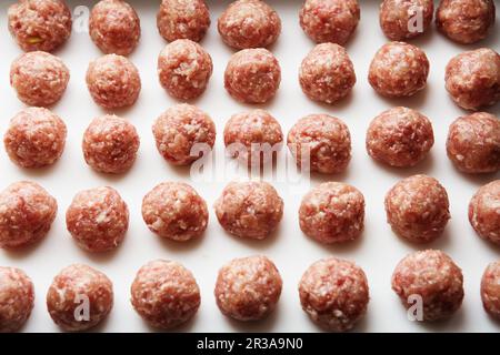 Freshly cooked raw meatballs lie on a white plastic kitchen board. Stock Photo