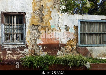 Facade of an old abandoned uninhabited house with destroyed plaster and bars on the windows Stock Photo