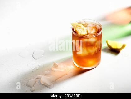 Ice cold iced tea with lemon wedges, drips on glass, colored shadows and melted ice Stock Photo