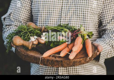 A man holding a wooden plater of freshly harvested vegetables Stock Photo