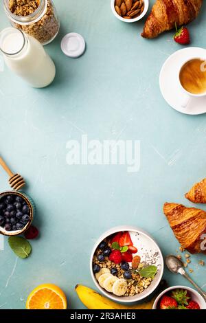 Breakfast with granola, yogurt, honey, fresh bananas, berries, chia seeds in bowl, coffee and croissants Stock Photo