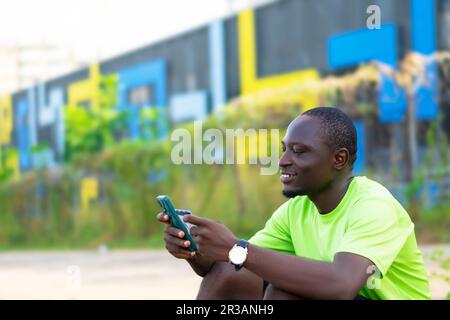 african black man smiling, seated using is mobile phone and credit card to make cashless transaction Stock Photo