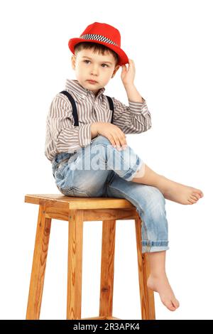 Portrait of a funny little boy sitting on a high stool in a red hat isolated on white background Stock Photo