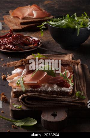 Cured ham in bread with goat's cheese, rocket and dried tomatoes Stock Photo