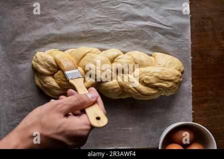 A braided loaf being spread with egg yolk Stock Photo