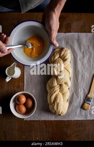 A braided loaf being spread with egg yolk Stock Photo