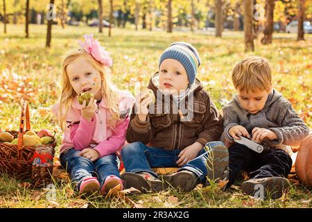 Three happy children playing in autumn park with fruits Stock Photo