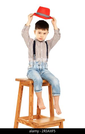 Portrait of a funny little boy sitting on a high stool in a red hat isolated on white background