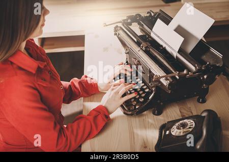Secretary at old typewriter with telephone. Young woman using typewriter. Business concepts. Retro p Stock Photo