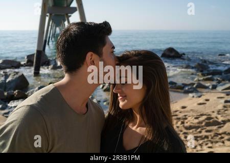 Young man kissing woman on forehead at beach Stock Photo