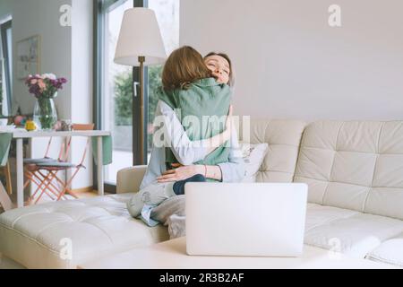 Mother hugging son sitting on sofa at home Stock Photo