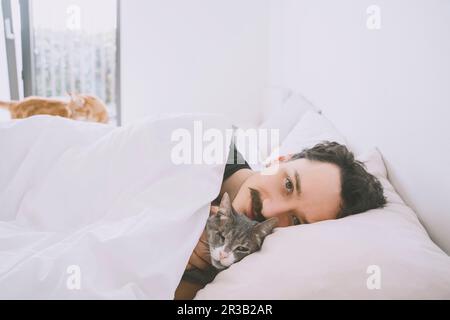 Smiling man relaxing on bed with cat at home Stock Photo
