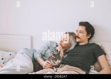 Thoughtful couple with cat lying on bed at home Stock Photo