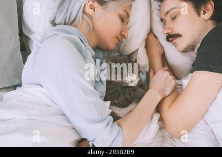 Couple with cat sleeping on bed at home Stock Photo