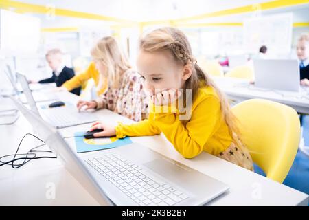 Blond schoolgirl learning through laptop in computer class Stock Photo