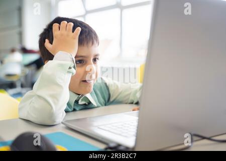 Schoolboy leaning on elbow using laptop in computer class Stock Photo
