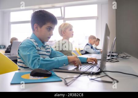 Boy doing E-learning through laptop sitting at desk in school Stock Photo