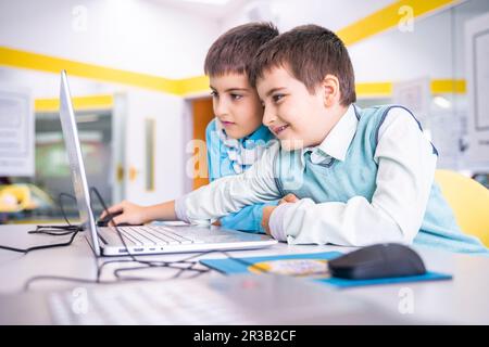 Smiling boy sharing laptop with friend at computer class in school Stock Photo