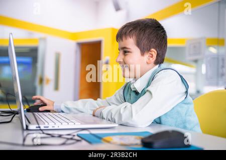 Smiling boy using laptop sitting at desk in school Stock Photo