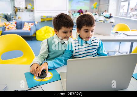 Boys sharing laptop sitting in computer class at school Stock Photo