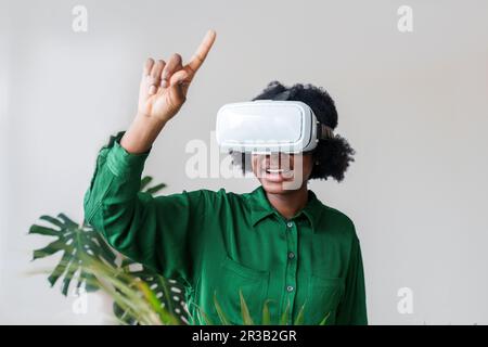 Smiling woman pointing finger and wearing virtual reality simulator Stock Photo