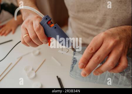 Father using hot glue gun for making plastic car at home Stock Photo