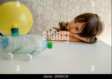 Boy looking at plastic bottle car leaning on table at home Stock Photo