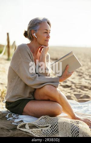 Thoughtful woman with hand on chin holding book at beach Stock Photo