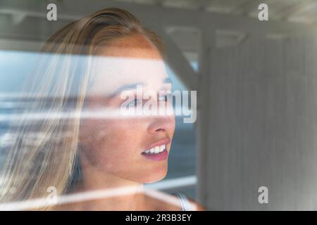 Thoughtful young woman looking through window Stock Photo