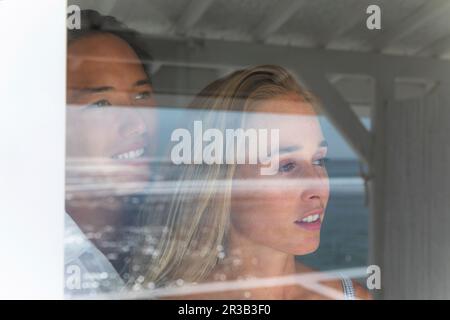 Smiling young couple looking through window Stock Photo
