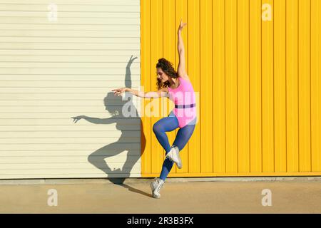 Young dancer showing ballet moves in front of yellow wall Stock Photo