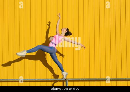 Carefree woman practicing ballet on railing in front of yellow wall Stock Photo