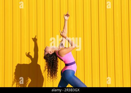 Young woman wearing bodysuit dancing in front of yellow wall Stock Photo