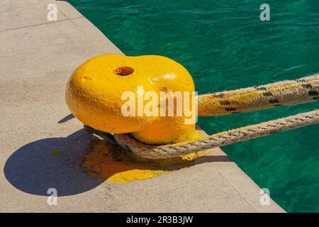 A thick hawser rope used to moor a ship on a yellow pier at the seaport. Stock Photo