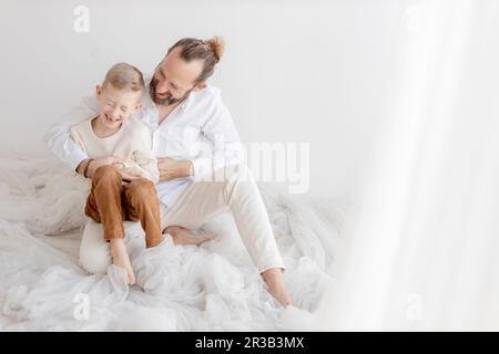 Man tickling son sitting near white wall Stock Photo