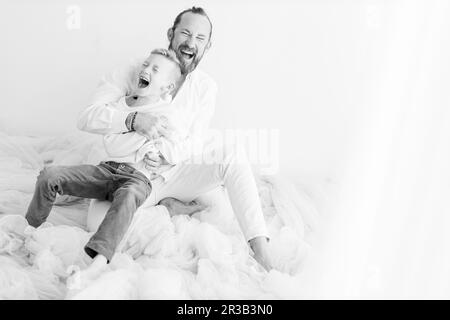 Happy man laughing with son sitting near wall Stock Photo