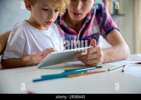 Father and son using tablet PC at desk Stock Photo