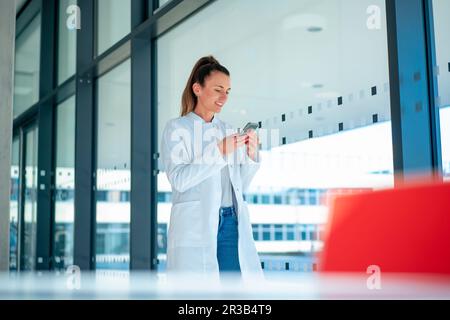 Smiling doctor using mobile phone standing in hospital Stock Photo