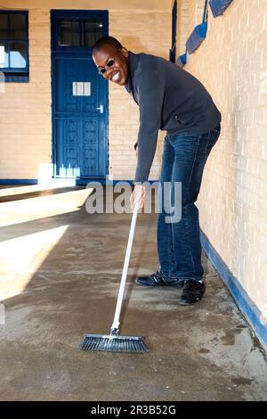 African man performing community service volunteer cleaning work at township school Stock Photo