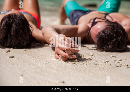 Couple holding hands lying on sand at beach Stock Photo