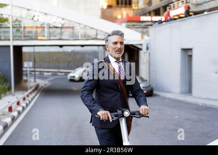 Mature businessman riding electric scooter on road Stock Photo