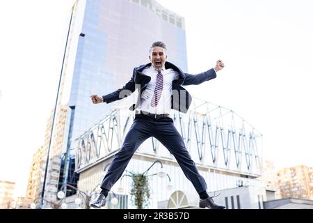 Excited businessman jumping in front of building Stock Photo