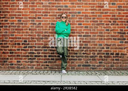 Teenage girl with arms crossed leaning on brick wall Stock Photo